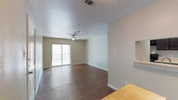 This single-floor residence offers a well-organized layout with a consistent neutral color palette and practical finishes throughout. The open living area is anchored by rich, dark hardwood-style flooring that extends through the main living spaces and kitchen, complemented by a ceiling fan with integrated lighting. A sliding glass door leads to a private balcony enclosed by a metal railing, allowing natural light to fill the room. A pass-through counter connects the living area to the kitchen, which features dark espresso-toned cabinetry, light granite-style countertops, and black appliances including a refrigerator, stovetop, and dishwasher. The bedrooms are carpeted in a warm neutral tone, each equipped with ceiling fans and windows fitted with blinds. One bedroom includes a walk-in closet with built-in shelving, offering ample storage. The bathroom features a full tub-shower combination with tile surround, dark wood cabinetry, and hardwood-style flooring. A separate entry area with hardwood-style floors and a front door with sidelight window provides a welcoming transition into the living space.