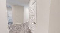 Located at 3061 Godwin Boulevard in Suffolk, Virginia, this single-floor residence showcases a thoughtfully designed, modern interior with a cohesive neutral color palette and quality finishes throughout. The open-concept kitchen serves as a central highlight, featuring granite countertops, white shaker-style cabinetry with brushed nickel hardware, a subway tile backsplash, stainless steel appliances, and a large island with an undermount sink. Pendant lighting and recessed ceiling lights provide both task and ambient illumination, while light wood-look flooring flows through the main living areas. A glass-panel exterior door and multiple windows dressed with white blinds invite natural light into the living and dining areas, creating a bright and airy atmosphere. The bedrooms are carpeted for comfort and are equipped with ceiling fans for year-round climate control. Multiple five-panel interior doors add a refined architectural detail throughout the home. A generously sized walk-in closet with wire shelving offers ample storage, and an en-suite bathroom is accessible directly from the primary bedroom. Connecting hallways are finished with the same light-toned hardwood-style flooring, maintaining a consistent and polished aesthetic from room to room.