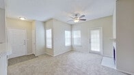 This single-floor residence offers a thoughtfully designed open-concept layout that connects the living, dining, and kitchen areas seamlessly. The spacious living room features plush carpeting, a ceiling fan with light fixture, a cozy fireplace, and multiple windows dressed with white blinds that invite generous natural light. A private exterior door provides direct outdoor access from the living space.

The kitchen is efficiently designed in a galley style, showcasing rich dark-wood cabinetry, light-toned countertops, wood-look flooring, and a full suite of black appliances including a refrigerator, range, microwave, and dishwasher. A breakfast bar with a pendant light overhead creates a natural transition between the kitchen and the adjoining dining or flex area.

The primary bedroom is carpeted and generously proportioned, offering a dedicated walk-in closet with built-in shelving and direct access to an en-suite bathroom. The en-suite features dark wood cabinetry, a stone-finish countertop, a large vanity mirror, and wood-look flooring. A second full bathroom includes a tub-shower combination with white tile surround, a single-sink vanity with matching cabinetry, and wood-look flooring. Throughout, neutral tones and clean finishes create a cohesive, move-in-ready aesthetic.