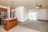 This single-floor residence offers a thoughtfully designed open-concept layout that seamlessly connects the kitchen, dining, and living areas. The kitchen is well-equipped with warm wood cabinetry, stainless steel appliances including a refrigerator, range, microwave, and dishwasher, complemented by a peninsula island ideal for casual dining or meal prep. Light wood-style flooring runs through the kitchen and entry areas, transitioning to plush carpet in the living and bedroom spaces. A ceiling-mounted chandelier and pendant lighting add a decorative touch, while a ceiling fan in the living area promotes airflow. Large sliding glass doors flood the living room with natural light and provide outdoor access. Bedrooms are generously sized, each featuring carpet flooring, ceiling fans or lighting fixtures, and windows for natural light. Closet space is plentiful, including a spacious walk-in closet with wire shelving. The bathroom includes a vanity with wood cabinetry, a tub/shower combination, and wood-style flooring. A dedicated in-unit laundry area houses a full-size washer and dryer. Throughout, warm-toned wood trim and neutral walls create a cohesive, comfortable atmosphere.