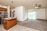 This single-floor residence offers a thoughtfully designed open-concept layout that seamlessly connects the kitchen, dining, and living areas. The kitchen is well-equipped with warm wood cabinetry, stainless steel appliances including a refrigerator, range, microwave, and dishwasher, complemented by a peninsula island ideal for casual dining or meal prep. Light wood-style flooring runs through the kitchen and entry areas, transitioning to plush carpet in the living and bedroom spaces. A ceiling-mounted chandelier and pendant lighting add a decorative touch, while a ceiling fan in the living area promotes airflow. Large sliding glass doors flood the living room with natural light and provide outdoor access. Bedrooms are generously sized, each featuring carpet flooring, ceiling fans or lighting fixtures, and windows for natural light. Closet space is plentiful, including a spacious walk-in closet with wire shelving. The bathroom includes a vanity with wood cabinetry, a tub/shower combination, and wood-style flooring. A dedicated in-unit laundry area houses a full-size washer and dryer. Throughout, warm-toned wood trim and neutral walls create a cohesive, comfortable atmosphere.