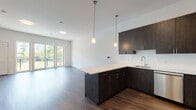 Located at 310 Madison in Elizabeth, NJ, this contemporary single-floor residence showcases a thoughtfully designed open-concept layout that seamlessly connects the kitchen, dining, and living areas. The kitchen is a standout feature, boasting dark wood-grain cabinetry with sleek bar-pull hardware, crisp white quartz countertops, a subway tile backsplash, and a central island ideal for meal preparation or casual dining. A full suite of stainless steel appliances — including a gas range, over-the-range microwave, dishwasher, and refrigerator — completes the modern culinary space. Pendant lighting above the island adds a refined touch. The living area is generously sized with hardwood-style flooring, bright white walls, and large glass sliding doors that open to a private balcony with outdoor views of lush greenery. Bedrooms benefit from oversized windows that flood the space with abundant natural light and offer views of the surrounding landscape. The bathroom is elegantly appointed with marble-patterned tile flooring and tub surround, a dark vanity with dual sinks, white quartz countertops, and a well-lit mirror. Throughout the unit, clean lines and a neutral palette create a cohesive, modern aesthetic.