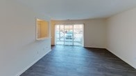 This single-story, one-bedroom, one-bathroom unit offers a practical and comfortable layout designed to maximize its well-proportioned footprint. The living area serves as the heart of the space, featuring durable wood-style plank flooring in a cool gray tone and a large sliding glass door fitted with vertical blinds, allowing an abundance of natural light to flow in while providing outdoor views. A pass-through window connects the living area to the kitchen, enhancing the open feel between the two spaces.

The kitchen is efficiently designed with white cabinetry extending to the upper walls for generous storage, white laminate countertops, a stainless steel double-basin sink, and white appliances including an electric range and dishwasher. The wood-style flooring continues seamlessly into this area.

The bedroom offers a quieter, carpeted retreat with a wide mirrored sliding-door closet providing ample storage, and a window dressed with vertical blinds for natural light and privacy. The full bathroom is finished with wood-style flooring, a single-sink vanity with a large mirror, and a shower-tub combination. A separate flex area adjacent to the bedroom provides additional versatile living space.