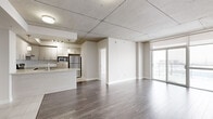 Located at 3410 Boul St-Elzéar O in Laval, QC, this two-bedroom, one-bathroom unit offers a thoughtfully designed open-concept layout. The combined living and kitchen area forms the heart of the space, where wood-look laminate flooring extends throughout, complemented by an exposed concrete ceiling that lends an industrial character to the otherwise clean, modern aesthetic.

The kitchen is well-appointed with light wood cabinetry, stainless steel appliances including a range, built-in microwave, and refrigerator, along with light-toned countertops and a white tile backsplash. A peninsula provides a natural divide between the kitchen and the living area.

The living area benefits from access to a private balcony through a sliding glass door, offering views of the surrounding Laval cityscape. Natural light filters generously into the space through large windows and the balcony entrance.

Both bedrooms feature the same wood-look flooring and neutral walls. The primary bedroom includes a large window with outdoor views, while the second bedroom offers a closet and similarly bright, understated finishes. A wall-mounted air conditioning unit serves the main living area, ensuring year-round comfort throughout this well-organized, contemporary unit.