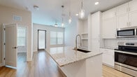 Located at 5701 Summerall Vista Circle in Riverview, FL, this single-floor unit offers a well-designed layout that makes efficient use of its intimate footprint. The kitchen serves as the centerpiece of the space, showcasing tall white shaker-style cabinetry extending to the ceiling, a granite-topped island with an undermount sink and pendant lighting, a full suite of stainless steel appliances including a refrigerator, electric range, and built-in microwave, and a classic white subway tile backsplash. Light wood-tone flooring runs throughout, lending warmth and continuity to the open-concept layout. A built-in shelving nook adds a functional architectural detail adjacent to the kitchen. The living area benefits from a ceiling fan, multiple windows with blinds that invite natural light, and direct access to an exterior door. The bathroom features neutral tile flooring, a granite-topped vanity with shaker cabinetry, and a large mirror, with direct access to a spacious walk-in closet outfitted with multi-level wire shelving along three walls — providing generous storage. A hallway connects the rooms, completing this clean, contemporary single-level layout designed for practical, comfortable everyday living.