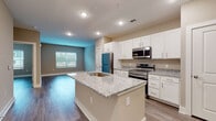 This thoughtfully designed single-floor residence offers a seamless open-concept layout that connects the kitchen, dining, and living areas into one cohesive space. The kitchen is a standout feature, showcasing crisp white shaker cabinetry, light granite countertops, and a central island with an undermount sink — ideal for both everyday cooking and entertaining. Stainless steel appliances, including a refrigerator, range, and over-the-range microwave, complete the kitchen's modern aesthetic. Wood-look plank flooring flows consistently throughout the entire unit, lending warmth and visual continuity to every room. The bedrooms are generously proportioned, each benefiting from natural light through large windows fitted with blinds. A ceiling fan in the primary bedroom adds comfort and functionality. The bathroom features a white vanity with granite countertops, a tub/shower combination, and light-toned wood-look flooring. A spacious walk-in closet equipped with wire shelving provides ample storage. Warm neutral wall tones, recessed lighting, and clean white trim work together to create a bright, welcoming atmosphere throughout this well-appointed space.