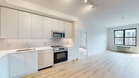 This thoughtfully designed 2-bedroom, 2-bathroom residence in Asbury Park, NJ offers a clean, modern aesthetic with light hardwood flooring and crisp white walls flowing throughout the single-floor layout. The open-concept living, dining, and kitchen area forms the heart of the home, anchored by a sleek kitchen outfitted with flat-front white cabinetry, a textured tile backsplash, white quartz countertops, and a full suite of stainless steel GE appliances including a French door refrigerator, electric range with over-the-range microwave, and dishwasher. Track lighting illuminates the space with a modern touch. Both bedrooms are generously proportioned, featuring large black-framed windows that invite abundant natural light and urban views, including a green roof terrace visible from one bedroom. The primary bedroom provides direct access to a private balcony. Closets are fitted with built-in shelving and hanging systems for ample storage. The bathrooms maintain the home's clean palette, with one featuring a soaking tub with built-in niche shelving. Additional conveniences include in-unit laundry, a utility room, and a welcoming hallway entry. The overall ambiance is bright, contemporary, and move-in ready.