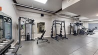 This fitness facility at 103 W College Ave in Appleton, Wisconsin, offers a thoughtfully designed exercise space that accommodates a wide variety of workout styles. The single-floor layout is divided into two distinct functional zones, each finished to support focused training.

The cardio area features a row of treadmills and stationary bikes by Spirit, positioned beneath bright flush-mounted ceiling lights. Large windows with roller shades allow natural light to filter in while providing privacy, and a wall-mounted flat-screen TV adds an entertainment option for cardio sessions. Light-toned tile flooring gives this section a clean, open feel.

The strength training area transitions to durable rubber tile flooring, providing the grip and cushioning needed for heavier workouts. This zone is comprehensively equipped with a Smith machine, cable cross machines, a multi-functional rack, adjustable weight benches, a full dumbbell rack, kettlebells, and a heavy punching bag with suspension gear for combat training. A large wall mirror reflects natural and artificial light, enhancing the sense of openness while allowing users to monitor their form.

Exposed ceiling elements and neutral gray-and-white walls give the space a modern industrial character. The layout is efficient yet spacious, providing ample room to move freely between stations. Overall, this facility delivers a complete fitness environment suitable for both cardio conditioning and serious strength training.