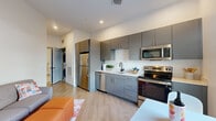 Located at 41 Seacoast Terrace in Kittery, Maine, this one-bedroom, one-bathroom residence offers a thoughtfully designed open-concept layout with modern finishes throughout. Light wood-tone flooring runs continuously through the living and kitchen areas, creating a warm, cohesive aesthetic.

The kitchen is well-appointed with sleek gray flat-front cabinetry, white countertops, and a full suite of stainless steel appliances, including a refrigerator, dishwasher, electric range, and microwave. A single-basin sink with a matte black faucet anchors the space, and recessed lighting provides clean, even illumination throughout. A dedicated in-unit laundry closet is conveniently accessible just off the kitchen area.

The living area flows naturally from the kitchen, offering a comfortable space for everyday use. The bedroom is a generously proportioned private retreat, featuring clean white walls, continued wood-tone flooring, and a paneled gray interior door with black hardware that adds a contemporary touch.

The bathroom is finished with large-format light gray tile flooring, a gray vanity, matte black hardware and towel bar, a full soaking tub with shower, and open wire shelving for added storage.

This residence combines functional design with modern, low-maintenance finishes, making it a practical and attractive home in coastal southern Maine.