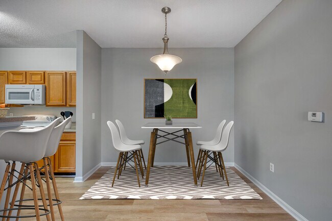 Vista de la sala de estar y la cocina en Dunwoody Place que muestra un plano de planta abierto con pisos de madera clara, muebles modernos, asientos en el mostrador a la altura de la barra y luz natural en un apartamento asequible en Huntsville, AL. - Dunwoody Place