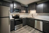 Located at 1567 Coleman Rd in Knoxville, Tennessee, this two-story home offers a thoughtfully updated interior with modern finishes throughout. Durable wood-look flooring runs across both levels, tying the spaces together with a cohesive, contemporary feel.

The kitchen is a standout feature, showcasing rich dark cabinetry paired with crisp white quartz countertops and a classic subway tile backsplash. A full suite of stainless steel appliances — including a refrigerator, range, microwave, and dishwasher — completes the space, making it as functional as it is visually striking.

An adjacent dining area benefits from a large sliding glass door that invites natural light and provides views of the outdoors, complemented by a modern geometric chandelier overhead. The main level also includes a well-appointed laundry room with a full-size washer and dryer and overhead storage cabinetry.

A staircase with white balusters and dark wood treads leads to the upper level, where bedrooms offer ample closet space and windows that bring in natural light. Bathrooms are finished with dark wood vanities, white countertops, and brushed nickel fixtures. A uniquely angled bathroom ceiling on the upper floor adds architectural character to the layout.