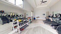 Located at 350 Joshua Pl NW in Concord, NC, this fitness center is a single-room exercise facility designed to support a well-rounded workout regimen. The space features soaring tray ceilings with crown molding detail, giving the room an open and airy feel, while a ceiling fan enhances comfort during workouts. Light-toned luxury vinyl plank flooring runs throughout, complementing the soft gray walls and white trim for a clean, modern aesthetic.

Large floor-to-ceiling windows and glass doors flood the space with abundant natural light and offer direct views of an outdoor pool and courtyard area, creating a refreshing and motivating atmosphere. Full-length wall mirrors along one side of the room visually expand the space and allow users to monitor their form during exercise.

The fitness center is equipped with a comprehensive selection of True-brand cardio machines, including treadmills, ellipticals, and a stair climber, all positioned to take advantage of the natural light and outdoor views. A multi-tiered dumbbell rack stocked with a wide range of free weights, along with colorful kettlebells, supports strength and functional training. A cable machine with an adjustable bench rounds out the strength equipment offerings. The space is accessible via double glass-panel doors and is thoughtfully organized to allow ample room for movement and exercise.