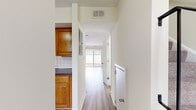 This 880-square-foot, two-bedroom, one-bathroom townhouse-style unit at Commons at Windsor Gardens in Norwood, MA is thoughtfully distributed across two floors. The ground floor (480 sq ft) features a combined kitchen and living room, a hallway, and staircase access. The living room is bright and open, finished with light hardwood-style flooring and neutral walls, with a sliding glass door providing natural light and access to a private outdoor patio area. The kitchen area includes a window with outdoor views and a pendant light overhead. The upper floor (400 sq ft) houses both bedrooms, the full bathroom, and a second staircase landing. Both bedrooms feature soft carpeting, neutral walls, and windows that bring in natural light with views of the surrounding greenery. Each bedroom includes a closet with a rod. The primary bedroom measures 170 sq ft. The full bathroom is clean and functional, featuring a tiled shower-tub combo, wood-look vinyl flooring, and brushed nickel fixtures. Throughout, the unit maintains a consistent, clean aesthetic with white trim, neutral tones, and practical finishes suited for everyday living.