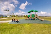 Located at 7063 Chestnut Hills Dr in Whitmore Lake, Michigan, this single-level outdoor community amenity space offers a well-planned recreational area designed to serve the surrounding residential neighborhood. The grounds are characterized by expansive, well-maintained green lawns that create an open and inviting atmosphere under the wide Michigan sky.

A standout feature is the covered picnic pavilion, a clean, modern structure with a sloped metal roof supported by white columns. Inside, multiple picnic tables provide ample seating, making it an ideal gathering spot for community events and outdoor dining. Gravel pathways wind through the grounds, connecting the pavilion to other areas of the space and offering a pleasant walking experience.

The dedicated children's playground is equipped with a multi-level play structure featuring slides, climbing elements, and soft rubber surfacing for safety. Benches are thoughtfully placed nearby for supervision and relaxation. Young trees have been planted throughout the grounds, suggesting a landscape designed to mature and provide additional shade and greenery over time.

Views from the amenity area look out toward the neighboring residential buildings, which feature neutral-toned siding and traditional rooflines. The community appears to be actively growing, with development visible in the background, reflecting a vibrant and expanding neighborhood.