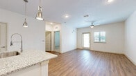 Located at 2950 Landover Blvd in Spring Hill, FL, this one-bedroom, one-bathroom residence offers a well-designed, single-floor layout that makes efficient use of its space. The open-concept kitchen and living area serves as the heart of the home, featuring warm wood-look flooring, a ceiling fan, and a glass door that leads to a private balcony, filling the space with natural light. The kitchen is a standout feature, appointed with white shaker-style cabinetry, a decorative tile backsplash, stainless steel appliances, granite countertops, and a central island with a built-in sink and stylish pendant lighting overhead. A dedicated pantry provides additional storage. The living area flows seamlessly from the kitchen and offers a bright, open feel. The bedroom is carpeted for comfort, benefits from natural light through dual windows, and includes a ceiling fan. A spacious walk-in closet with built-in wire shelving provides generous storage. The bathroom is well-appointed with a granite-topped vanity, a large framed mirror, wood-look flooring, and a tub-shower combination. Additional conveniences include a dedicated laundry area, completing this thoughtfully arranged home.