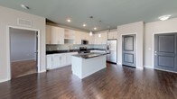 This single-floor, 2-bedroom, 2-bathroom residence delivers a thoughtfully designed open-concept layout with a clean, modern aesthetic. The kitchen serves as the centerpiece of the living area, featuring white shaker-style cabinetry, dark granite countertops, a subway tile backsplash, and a full suite of stainless steel appliances including a refrigerator, range, and microwave. A central island with matching dark countertop provides additional prep and seating space, while pendant lighting above and recessed lighting throughout create a bright, welcoming atmosphere. Rich dark hardwood-style flooring extends seamlessly through the main living areas, adding warmth and continuity.

Both bedrooms offer plush carpeting, neutral gray walls, and windows that allow natural light to filter in. The primary bedroom includes a ceiling fan, a spacious walk-in closet, and direct access to its en-suite bathroom. The primary bath features a dual-sink vanity with dark countertops, white cabinetry, and a soaking tub with a shower surround. The second bathroom is equally well-finished, with a clean tub-shower combo and hardwood-style flooring. The overall color palette of soft grays, crisp whites, and dark accents gives the home a cohesive, contemporary feel throughout.
