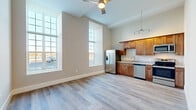 Located on Dwelly Street in Fall River, MA, this one-bedroom, one-bathroom unit offers a well-designed, efficiently laid-out living space across a single floor. The open living area immediately impresses with soaring ceilings, a ceiling fan, and oversized grid-pane windows that flood the space with abundant natural light while framing views of the surrounding area. Light-toned hardwood-style flooring runs continuously throughout, creating a cohesive and clean aesthetic.

The kitchen is well-appointed with warm wood cabinetry, granite countertops, and a full suite of stainless steel appliances, including a French door refrigerator with ice maker, electric range, built-in microwave, and dishwasher. A track lighting fixture overhead ensures excellent task illumination. The kitchen flows naturally into the living area, making the space feel open and connected.

The bedroom is a comfortable, quiet retreat with neutral walls, hardwood-style flooring, and access to a walk-in closet with built-in wire shelving. The full bathroom features a wood-toned vanity with granite countertop, a tub/shower combo, and the added convenience of an in-unit stacked washer and dryer. Hallways connect the rooms efficiently, completing this practical and modern living space.