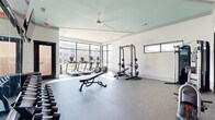 Located at 2200 Cascade Pointe Blvd in Charlotte, NC, this fitness center is a thoughtfully designed exercise facility offering a comprehensive workout environment across a single floor. The space is divided into two distinct zones connected by glass-framed doors with sleek black trim.

The main workout area features durable rubber flooring and is flooded with natural light through expansive floor-to-ceiling windows along the corner wall, offering outdoor views of the surrounding community. This area is equipped with multiple treadmills, an elliptical, a rowing machine, a full power rack with a bench press station, adjustable benches, and a full dumbbell rack. A large ceiling fan with a mint-accented ceiling adds comfort and visual interest, while wall-mounted flat-screen TVs ensure entertainment during workouts. Mirrors line portions of the walls to enhance the sense of space.

An adjacent studio room features warm hardwood-style flooring, full-length mirrors, mounted TVs, and clerestory windows that allow natural light while maintaining privacy. This room is ideal for stretching, yoga, or group fitness. A standout feature is the vibrant abstract mural accent wall near the entryway, which adds an artistic, energizing touch alongside a rack of medicine balls and kettlebells. Together, these spaces create a modern, fully functional fitness facility.