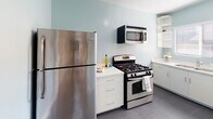 Located at 990 Palm Ave in the heart of West Hollywood, this single-story unit offers a clean and functional layout with a cohesive, understated aesthetic throughout. The living area is finished with warm hardwood flooring that extends through the main spaces, complemented by crisp white walls and a wall-mounted heater unit. Natural light filters through the space, contributing to a bright and open feel. A doorway connects seamlessly to adjacent rooms, maintaining a practical and easy-to-navigate floor plan. The kitchen is efficiently designed, featuring light blue-toned walls, white cabinetry, and a white countertop with a double-basin stainless steel sink positioned beneath a window that allows in natural light. Stainless steel appliances include a gas range, over-the-range microwave, and a full-size refrigerator, offering a well-equipped cooking space. A hallway leads to the bathroom, which is accessed through a frosted glass-paneled door for added privacy. The bathroom is finished with dark tile flooring, a pedestal sink, toilet, and a shower-tub combination with a window providing natural ventilation. An electrical panel is conveniently accessible in the hallway. Overall, the unit presents a tidy, move-in ready space in a prime West Hollywood location.