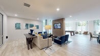 Located in Memphis, TN, this single-floor club lounge offers a generously sized, open-concept layout designed for community gathering and leisure. The space features light wood-look tile flooring throughout, recessed lighting, and a neutral color palette punctuated by bold navy and teal accents in the furnishings and artwork.

The main lounge area is anchored by a neutral sectional sofa paired with navy accent chairs arranged around a central coffee table, with a wall-mounted flat-screen TV set into a warm wood-paneled feature wall. Large floor-to-ceiling windows flood the space with natural light and provide views of surrounding greenery, enhancing the open, airy atmosphere.

A dedicated game area accommodates a full-size pool table beneath a chandelier, with additional casual seating nearby. A glass-walled private room with sliding panel doors offers a more enclosed setting for meetings or small gatherings.

The lounge also includes a kitchen-style bar area featuring a stone-accented backsplash, white cabinetry, a sink, and globe pendant lighting over a communal high-top table with striped barstools. A dedicated coffee bar station with teal accent wall and neon signage adds a stylish, functional touch to the overall space.
