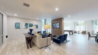 Located in Memphis, TN, this single-floor club lounge offers a generously sized, open-concept layout designed for community gathering and leisure. The space features light wood-look tile flooring throughout, recessed lighting, and a neutral color palette punctuated by bold navy and teal accents in the furnishings and artwork.

The main lounge area is anchored by a neutral sectional sofa paired with navy accent chairs arranged around a central coffee table, with a wall-mounted flat-screen TV set into a warm wood-paneled feature wall. Large floor-to-ceiling windows flood the space with natural light and provide views of surrounding greenery, enhancing the open, airy atmosphere.

A dedicated game area accommodates a full-size pool table beneath a chandelier, with additional casual seating nearby. A glass-walled private room with sliding panel doors offers a more enclosed setting for meetings or small gatherings.

The lounge also includes a kitchen-style bar area featuring a stone-accented backsplash, white cabinetry, a sink, and globe pendant lighting over a communal high-top table with striped barstools. A dedicated coffee bar station with teal accent wall and neon signage adds a stylish, functional touch to the overall space.