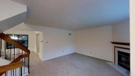 This three-floor property offers a versatile layout spread across multiple levels, providing ample separation of living spaces. The image reveals a spacious, carpeted room with neutral wall tones and smooth ceilings, creating a clean and understated aesthetic. The light grey carpet provides a soft, uniform flooring surface throughout the room, contributing to a quiet and comfortable atmosphere. HVAC vents are integrated into both the ceiling and walls, ensuring climate control throughout the space. An open doorway leads to an adjoining area, suggesting a connected and functional floor plan. Electrical outlets and switch plates are conveniently positioned along the walls. The room's generous proportions allow for flexible furniture arrangements to suit a variety of uses. The overall design of the space prioritizes simplicity and practicality, with white walls that offer a blank canvas for personalization. With three floors in total, the property provides distinct zones for living, sleeping, and utility purposes, making it a well-structured and adaptable space suited to a range of occupants and lifestyles.