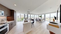 This contemporary high-rise unit showcases a thoughtfully designed open-concept layout finished in a clean, neutral palette throughout. Light hardwood flooring extends across the main living areas, complementing the bright white walls and ceilings. Floor-to-ceiling windows wrap around the living and dining areas, flooding the space with natural light and offering sweeping panoramic views of the surrounding cityscape and greenery below.

The kitchen is outfitted with rich wood-grain cabinetry, a white quartz countertop, a subway tile backsplash, and a full suite of stainless steel appliances including a gas range, built-in microwave, and a large French-door refrigerator. A central island with seating provides an ideal space for casual dining or entertaining.

The living area is generously proportioned, with corner window placement maximizing views from multiple angles. Both bedrooms are well-sized, featuring large windows that frame urban vistas and bring in ample daylight. The primary bathroom includes a frameless glass walk-in shower with a rainfall showerhead, while the secondary bathroom offers a tub-shower combination. The overall ambiance is modern, airy, and refined throughout.