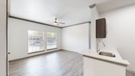 This 1-bedroom, 2-bathroom single-floor residence offers a thoughtfully designed layout that maximizes every inch of its compact footprint. Light gray wood-look flooring runs consistently throughout, creating a cohesive and modern aesthetic. Crown molding with dark wood accents adds a polished architectural detail to the living areas and bedroom.

The open-concept living room is bright and airy, featuring large windows that invite generous natural light and views of surrounding greenery. A ceiling fan overhead adds both function and style. The space flows naturally into the kitchen, which is equipped with dark espresso cabinetry, stainless steel appliances including a refrigerator and over-the-range microwave, a black gas range, and a peninsula with a stainless steel sink and light-toned countertop — ideal for casual dining or food prep.

The bedroom is comfortably sized, offering dual windows for ample daylight, a ceiling fan, and direct access to a walk-in closet, providing generous storage. A private exterior door with sidelights adds convenience and additional light. The two bathrooms are clean and functional, with one featuring a full tub-shower combination with white tile surround, wood-look flooring, and a dark wood vanity. Two dedicated closets further enhance the storage capacity of this well-organized home.