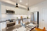 Located at 4700 Hampden Lane in the heart of Bethesda, MD, this well-appointed two-bedroom, two-bathroom residence offers a thoughtfully designed single-level layout with approximately 930 square feet of comfortable living space. Warm hardwood floors flow throughout, lending a cohesive and inviting character to every room.

The open-concept kitchen is a standout feature, equipped with full stainless steel appliances including a gas range, dishwasher, and large refrigerator. Crisp white cabinetry extends to the ceiling, complemented by a classic subway tile backsplash and dark countertops. A kitchen island with seating for two and stylish pendant lighting makes the space equally functional and visually striking.

The living room offers generous natural light through large windows, framing urban views of Bethesda's skyline. The bright, neutral palette creates a calm and welcoming atmosphere throughout.

Both bedrooms are comfortably sized, with the primary bedroom featuring multiple windows that fill the room with natural light and offer city views. Each room benefits from dedicated closet space.

The two bathrooms are finished with classic black-and-white mosaic tile floors. One bathroom features a soaking tub with subway tile surround, while the other includes a marble-topped vanity, both maintaining a clean, timeless aesthetic throughout.