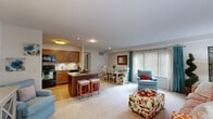 This thoughtfully designed 2-bedroom, 2-bathroom single-floor residence offers a comfortable and functional layout ideal for everyday living. The open-concept kitchen, dining, and living area serves as the heart of the home, creating a seamless flow between spaces. The kitchen is outfitted with warm honey-toned wood cabinetry, granite countertops, a tile backsplash, and black appliances including a refrigerator, range, built-in microwave, and dishwasher. A peninsula with bar seating provides additional prep and dining space, while hardwood-style flooring grounds the kitchen area. The combined dining and living room is carpeted and bathed in natural light from large windows dressed with teal drapes and horizontal blinds, creating a bright and inviting atmosphere. The spacious primary bedroom features plush carpeting, a wide window with natural light, and ample room for a full furniture suite. The second bedroom is equally carpeted and versatile, suitable as a guest room or home office. Both bathrooms are clean and functional, with one featuring a full tub-shower combination. A hallway connects the private quarters to the main living areas, completing this well-organized and comfortable floor plan.