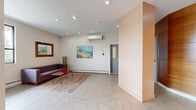 Located at 160 Pinehouse Dr in Saskatoon, Saskatchewan, this single-floor common area serves as the welcoming lobby and lounge for the building. The space is finished with large-format ceramic tile flooring laid in a diagonal chevron pattern, lending a clean and contemporary aesthetic throughout.

The living and lounge area is furnished with a tufted grey sofa, a hairpin-leg coffee table, and a colorful woven area rug, creating an inviting seating space for residents. A large grid-style window allows natural light to fill the room and offers views of the surrounding greenery. A framed mirror and a vibrant landscape painting add warmth to the neutral walls, while a wall-mounted split air conditioning unit and baseboard heating ensure year-round comfort.

The lobby area features a striking curved accent wall clad in warm wood paneling, which extends to house a built-in bank of individual mailboxes — a practical and visually cohesive design element. Recessed pot lighting is used throughout, providing consistent, even illumination. Additional accent walls in a terracotta-orange tone punctuate the space and complement the natural wood finishes. Elevator access and secondary entry doors are clearly integrated into the layout, making this lobby both functional and architecturally refined.
