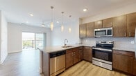 Located at 8137 Wisteria Pl in Norfolk, Virginia, this contemporary single-floor residence offers a thoughtfully designed open-concept layout with modern finishes throughout. The kitchen serves as a central highlight, featuring rich dark-wood cabinetry, granite-style countertops, a tiled backsplash, and a full suite of stainless steel appliances including a range, over-the-range microwave, dishwasher, and refrigerator. A peninsula with pendant lighting connects the kitchen seamlessly to the living area, which is finished with light luxury vinyl plank flooring and a ceiling fan. Sliding glass doors lead from the living area to a private balcony, offering open outdoor views. The bedrooms are carpeted for comfort, with one featuring a large walk-in closet with built-in shelving and another showcasing a wide window array that fills the room with natural light. The bathroom is well-appointed with wood-look flooring, a tub-shower combination, and brushed nickel fixtures. A hallway with ample closet storage and consistent luxury vinyl plank flooring ties the unit together, creating a bright, cohesive, and functional living environment.