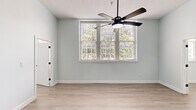Located at 1003 Elmwood Ave in Columbia, SC, this single-floor unit offers a clean, modern aesthetic defined by soft sage-green walls, light-tone luxury vinyl plank flooring, and crisp white trim throughout. The combined kitchen and living area forms the heart of the home. The galley-style kitchen is outfitted with white shaker cabinets accented by matte black hardware, quartz countertops, a stainless steel undermount sink with a coiled pull-down faucet, and a full suite of stainless steel appliances including a refrigerator, electric range, and over-the-range microwave. The living area is bright and open, benefiting from generous natural light. The bedroom is a comfortable, well-proportioned retreat featuring a trio of large windows with views of surrounding greenery, a ceiling fan with integrated light fixture, and a textured ceiling detail. The bathroom is thoughtfully finished with a white shaker vanity, quartz countertop, matte black fixtures, a framed mirror, and a tub-shower combination with white tile surround. Consistent flooring, a neutral color palette, and cohesive matte black accents give the entire space a polished, unified character.