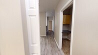 Located at 1200 Bismark Lane SE in Lacey, Washington, this single-floor unit offers a thoughtfully designed layout suited for comfortable everyday living. The open-concept living area is finished with light wood-style luxury vinyl plank flooring and is bathed in natural light through large windows fitted with horizontal blinds, with a door providing direct outdoor access. The kitchen is efficiently arranged with warm-toned wood cabinetry, dark granite-style countertops, and stainless steel appliances including a refrigerator, over-the-range microwave, and an electric range. A hallway connects the main living spaces, with a convenient built-in shelving nook visible along the corridor. The bedrooms feature plush carpeting and neutral-toned walls; one bedroom includes a mirrored sliding closet, while another offers a window with views of surrounding greenery and a baseboard heater. The unit includes two bathrooms: a full bath with a soaking tub and shower combination accented by white tile surround and a brushed nickel grab bar, and a half or secondary bath featuring a single-basin vanity with granite-style countertops, warm wood cabinetry, and light vinyl plank flooring. The overall ambiance is clean, neutral, and move-in ready.