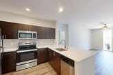 This single-floor unit is part of a contemporary multi-unit residential community, distinguished by its bold exterior color accents, clean stucco facades, and a well-maintained courtyard with landscaped planters and communal seating areas. The unit accommodates four bedrooms and two full bathrooms across a efficiently laid-out floor plan.

The kitchen is equipped with stainless steel appliances—including a range, microwave, and dishwasher—paired with rich dark-wood cabinetry and white countertops. A peninsula with an undermount sink extends into the living area, creating an open, connected feel. Light wood-style flooring runs consistently throughout the unit, contributing to a clean and cohesive aesthetic.

The primary bedroom offers a comfortable footprint, a dedicated closet, and direct access to a bathroom featuring a dark vanity cabinet and a tub-shower combination. Additional bedrooms are well-proportioned, each with a ceiling fan and natural light from windows. One bedroom provides sliding glass door access to a private balcony with courtyard views. The second bathroom mirrors the first in its clean, functional design with a tub-shower unit and wood-tone vanity.