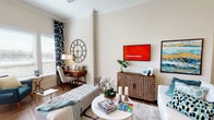 This two-bedroom, two-bathroom residence is thoughtfully designed across a single floor, offering a spacious and cohesive layout well-suited for modern living. The living room serves as the heart of the home, featuring tall ceilings accented by crown molding, warm hardwood-style flooring, and an abundance of natural light filtered through large windows dressed with patterned drapes. The open, airy atmosphere is complemented by neutral wall tones that provide a versatile backdrop throughout.

The dining area is distinctly defined, accommodating a round dining table with ample seating, and is adorned with decorative wall art that adds character to the space. The kitchen, visible in the floor plan, connects fluidly to the dining and living areas.

Both bedrooms are generously proportioned. The primary bedroom features plush carpeting, large windows offering natural light, a ceiling fan, and ample room for substantial furnishings. The bathrooms are finished with light tile flooring and tile-surround soaking tubs, offering a clean and polished aesthetic.

A dedicated laundry room with full-size washer and dryer hookups adds everyday convenience. Throughout the residence, consistent finishes and well-considered details create a cohesive and comfortable living environment.
