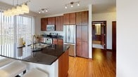 Located at 3115 Lilly Rd in Brookfield, Wisconsin, this single-floor residence offers a well-designed, open-concept layout that seamlessly connects its living, dining, and kitchen areas. The kitchen is a standout feature, boasting rich dark-stained wood cabinetry extending to the ceiling, dark granite countertops, stainless steel appliances including a French door refrigerator, and track lighting overhead. Hardwood flooring flows through the kitchen and dining area, where a sliding glass door with vertical blinds invites natural light and outdoor views. The living room is generously proportioned, wrapped in large windows with horizontal blinds that flood the space with daylight and provide views of the surrounding landscape. Plush carpeting adds warmth to the living areas and bedrooms. The bedrooms are well-sized, featuring neutral walls, carpeted floors, and windows offering outdoor views. Two bathrooms serve the unit — one with a full soaking tub and shower combination with brushed nickel fixtures, and a second featuring a glass-enclosed walk-in shower and a dark wood vanity with stone countertops. Throughout the residence, clean white walls, dark wood baseboards, and consistent finishes create a cohesive and modern aesthetic.