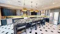 Located at 13325 Station Rail Way in Middletown, Kentucky, this single-floor amenity space is designed to impress with a cohesive blend of bold design choices and functional layouts. The centerpiece of the space is a generously sized gourmet kitchen, showcasing a dramatic black and white veined granite island with seating for multiple guests, dark cabinetry with glass-front upper shelves, a vibrant yellow-green subway tile backsplash, stainless steel appliances including a range and hood vent, and striking brass pendant lighting overhead. The signature black-and-white diamond-patterned tile flooring flows seamlessly throughout the space, creating a unified aesthetic. The open lounge area features bold red tufted leather armchairs arranged around a substantial wood coffee table, with large floor-to-ceiling windows and glass doors providing expansive outdoor views and flooding the interior with natural light. A semi-private seating nook adorned with decorative botanical wallpaper and a glass-walled conference or dining room offer flexible gathering options. Additional seating areas near the exterior access points further extend the functionality of the space, making it well-suited for both casual socializing and organized events.