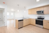This well-designed single-floor unit offers a clean, contemporary aesthetic throughout. The open-concept layout seamlessly connects the kitchen and living area, creating a bright and functional shared space. The kitchen is a standout feature, outfitted with flat-front light wood cabinetry, a white subway tile backsplash, a light-toned countertop peninsula, and a full suite of stainless steel appliances including an electric range, over-the-range microwave, dishwasher, and refrigerator. Pendant lighting above the peninsula adds a modern touch, while recessed ceiling lights provide ample illumination across the cooking and dining area.

The living area extends naturally from the kitchen, benefiting from the same light wood laminate flooring that runs throughout the main living spaces. The open layout and neutral white walls contribute to a clean, airy ambiance.

The bedrooms are carpeted or finished with light wood flooring and feature large windows fitted with blinds, allowing generous natural light and views of the surrounding neighborhood. The rooms are well-proportioned with clean lines and neutral tones.

The bathroom is finished with a full-size soaking tub and shower combination, a wood-trimmed vanity, and light wood flooring, maintaining the consistent, understated style found throughout the unit. Overall, the space presents a modern, move-in-ready design with practical finishes and a cohesive, light-filled atmosphere.
