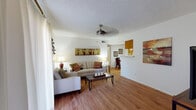 This single-story residence offers a thoughtfully organized layout that balances comfort and functionality throughout its interconnected rooms. The living room serves as the heart of the home, featuring warm hardwood-style flooring, a textured ceiling with a ceiling fan, and a large sliding glass door dressed with sheer vertical blinds that draw in generous natural light. The space accommodates both a seating and lounging area, creating an open, welcoming atmosphere.

Adjacent to the living room, the dining area provides a cozy setting with hardwood-style flooring continuing underfoot and ample wall space accented by framed artwork. A galley-style kitchen runs parallel to the main living spaces, outfitted with warm wood cabinetry, white countertops, stainless steel appliances including a refrigerator, and a double-basin sink — all set over light hardwood-style flooring.

The bedrooms offer plush carpeting, multiple windows with sheer curtains for soft natural light, and textured ceilings. Both bathrooms are finished with wood-toned cabinetry, white countertops, large mirrors, and hardwood-style flooring. One bathroom features a tub-shower combination, while the other presents a more streamlined vanity configuration, rounding out this cohesive and livable residence.