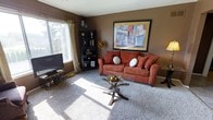 This single-floor residence features a thoughtfully arranged layout that maximizes its comfortable footprint across four distinct areas. The living room serves as the heart of the home, finished with plush carpeting and warm earth-toned walls that create an inviting atmosphere. A large window allows natural light to fill the space, complementing the cozy seating area centered around a glass-top coffee table. Bold wall art adds a decorative focal point to the room.

Adjacent to the living area, the dining space accommodates a glass-and-metal table with seating for four, positioned conveniently near the kitchen for easy entertaining. The kitchen is efficiently designed with white cabinetry, light countertops, a double sink, and tile flooring. Appliances including a refrigerator and range are seamlessly integrated into the layout.

The bedroom is a well-proportioned retreat featuring soft carpeting, a large window dressed with curtain panels that invite natural light, and ample space for a full furniture arrangement including a dresser and nightstands. Throughout the residence, the consistent warm brown palette and tile-to-carpet transitions create a unified, welcoming ambiance.