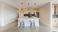 Located at Platinum in Sioux Falls, South Dakota, this thoughtfully designed single-floor residence offers a seamless blend of modern aesthetics and functional living. The open-concept kitchen and living area serves as the heart of the home, anchored by polished concrete floors that run throughout. The kitchen features light maple cabinetry, a bold dark subway tile backsplash, stainless steel appliances, and a generously sized waterfall island with bar seating illuminated by three pendant lights overhead. The adjoining living room exudes warmth with a floor-to-ceiling tile-surround fireplace and large black-framed windows that invite natural light. The primary bedroom is a serene retreat, complete with a ceiling fan, a large black-framed window, and two closets — including a walk-in with built-in shelving and hanging storage. The three bathrooms are consistently appointed with light wood vanities, white quartz countertops, and sleek matte black hardware and fixtures. A dedicated office provides a bright, versatile space with concrete flooring and a ceiling fan. A utility room rounds out the layout, adding practical convenience. The cohesive use of neutral tones, matte black accents, and clean lines gives this residence a distinctly contemporary character.