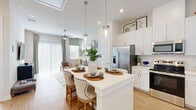 Located at 200 Villas Dr in Lavon, TX, this single-story home offers a well-appointed one-bedroom, one-bathroom layout designed for comfortable, efficient living. The open-concept floor plan seamlessly connects the kitchen, dining area, and living room, creating a cohesive and inviting atmosphere throughout.

The kitchen is a standout feature, showcasing crisp white cabinetry that extends to the ceiling, a full suite of stainless steel appliances including a French door refrigerator, gas range, microwave, and dishwasher, along with a large white quartz island with bar seating illuminated by sleek pendant lighting. Light hardwood-style flooring flows throughout the common areas, enhancing the bright, airy feel.

The living room is bathed in natural light from floor-to-ceiling sliding glass doors dressed with vertical blinds and a ceiling fan overhead. The bedroom is a serene retreat with natural light filtering through blinds and drapes, offering ample room for furnishings. The walk-in closet provides generous hanging space and built-in shelving for organized storage.

The bathroom features a clean white vanity with a single-sink, a large mirror, and a glass-enclosed walk-in shower with tile surround. An in-unit laundry area adds everyday convenience to this well-rounded home.