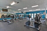 Located at 4946 Snapfinger Woods Dr in Decatur, Georgia, this single-floor fitness center is designed to provide a comprehensive workout environment. The space is defined by its bold teal and white color scheme, with motivational words such as "strength," "dedication," "focus," and "change" displayed prominently along the upper walls and large mirrors, creating an energizing atmosphere throughout.

The main workout area is generously sized, featuring durable rubber flooring and a full lineup of cardio equipment including multiple treadmills and stationary bikes. A dedicated strength training section houses a variety of resistance machines and a dumbbell rack, catering to a wide range of fitness routines. Large mirrors along the walls amplify the sense of space and allow for proper form checks during exercise. A wall-mounted television provides entertainment for cardio sessions.

A standout feature of this facility is the enclosed racquetball court, accessed through glass panel doors. The court boasts a hardwood floor and offers an exciting alternative to traditional gym workouts. Natural light filters into the space through multiple exterior-facing doors and windows, contributing to an open and inviting feel. Stone-accented partition walls add a distinctive architectural touch, complementing the contemporary design. The facility is well-lit with overhead fluorescent lighting throughout.