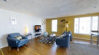 This single-floor, 3-bedroom, 3-bathroom residence offers a well-designed layout that balances comfort and functionality. The living room serves as the heart of the home, featuring rich hardwood-style flooring that extends throughout the space, adding warmth and visual continuity. A textured ceiling and crisp white walls provide a clean backdrop, while a bold mustard-yellow accent wall introduces a striking pop of color and personality to the room. Large windows along the exterior wall flood the space with natural light, creating a bright and airy atmosphere. The living area is generously proportioned, easily accommodating multiple seating arrangements centered around a sleek entertainment setup. Decorative wall accents and tasteful furnishings contribute to a modern yet inviting ambiance. The open feel of the living space flows naturally, making it ideal for both everyday living and entertaining. With three full bathrooms complementing the three bedrooms, this residence provides ample space and privacy for residents. The single-floor layout ensures seamless accessibility throughout, making it a practical and comfortable place to call home.
