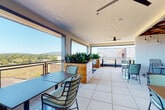This contemporary rooftop amenity space is designed to offer both comfort and style across a thoughtfully laid-out single level. Large-format tile flooring flows seamlessly throughout the interior and covered outdoor terrace areas, creating a cohesive and expansive feel.

The open-air terrace is a standout feature, framed by wide openings and modern metal railings that invite sweeping views of the surrounding skyline, rolling hills, and neighboring rooftops. Ceiling fans keep the covered outdoor sections comfortable, while raised planters filled with lush tropical greenery add a natural, vibrant element to the space.

Inside, a granite-topped bar counter anchors one area, illuminated by a cluster of pendant lights hanging from the ceiling. Nearby, built-in bench seating with green cushions provides a relaxed social setting. Multiple seating arrangements with sleek metal chairs and tables are positioned throughout both the indoor and outdoor zones, accommodating groups of various sizes.

A dedicated media lounge features one of the most distinctive design elements: an ornate coffered wood ceiling with a rich lattice pattern, paired with white subway tile walls and warm pendant lighting. High bar-height tables with wooden stools and a wall-mounted display screen make this room ideal for gatherings or presentations.

Throughout the space, bold abstract artwork, thoughtful lighting, and an abundance of natural light contribute to a refined yet welcoming atmosphere.