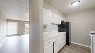 This 2-bedroom, 1-bathroom single-floor unit offers a practical and comfortable layout with consistent wood-look flooring and neutral warm-gray tones throughout. The combined kitchen and living area forms the heart of the space, with the kitchen featuring white cabinetry, marble-pattern countertops, a black refrigerator, a white electric range, and a pass-through window that connects to the living room. The living room is generously proportioned, bathed in natural light from a sliding glass door that opens onto a private balcony, providing outdoor views and additional brightness. A textured ceiling is present throughout the unit, adding a classic touch to the interior. The primary bedroom is a well-sized, light-filled room with hardwood-style flooring and a window fitted with blinds, while the second bedroom is similarly finished with its own window. The primary bedroom features dual closets, offering ample storage. Hallways connect the rooms efficiently, with an additional closet providing further storage options. The full bathroom includes a tiled tub-shower combination, a toilet, and wood-look flooring. Overall, the space presents a clean, functional, and cohesive living environment.