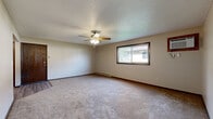 Located at 1625 Commerce Dr in North Mankato, Minnesota, this 2-bedroom, 1-bathroom unit offers a functional and straightforward layout across a single floor. The combined kitchen and living room serves as the heart of the space, with the kitchen featuring warm oak cabinetry extending to the ceiling for ample storage, light countertops, wood-look vinyl flooring, and white appliances including a refrigerator, range, and over-the-range microwave. The living area transitions to soft carpet and includes a wood-paneled entry door, baseboard heating, and a textured ceiling throughout. The primary bedroom is generously sized, offering a ceiling fan with light fixture, a wall-mounted AC unit, a window with outdoor views of surrounding greenery, and a full-size closet with dark wood bi-fold doors. The second bedroom features carpeted flooring, a window with blinds for natural light, and baseboard heating. The bathroom is clean and well-appointed with a tub-shower combination, a dark-cabinet vanity with a white countertop, and wood-look vinyl flooring. Neutral beige tones, dark wood trim, and textured ceilings are consistent throughout, giving the space a cohesive and understated character.