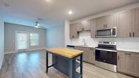 Located at 464 S Kirkman Rd in Orlando, Florida, this thoughtfully designed single-floor residence offers a clean, contemporary aesthetic throughout. The open-concept kitchen is a standout feature, showcasing warm-toned shaker-style cabinetry, a classic white subway tile backsplash, light quartz countertops, and a full suite of stainless steel appliances including a refrigerator, electric range, microwave, and dishwasher. A freestanding kitchen island with a butcher block top and navy base adds both style and functionality to the space. Light wood-style flooring runs throughout the main living and kitchen areas, creating a bright and cohesive feel, while recessed lighting and a ceiling fan enhance comfort and illumination. The bedrooms are carpeted for warmth and comfort, each featuring neutral gray tones, natural light from windows with blinds, and ceiling fans for climate control. The bathroom is well-appointed with a wide-format vanity mirror, wood-grain cabinetry, a white quartz countertop, and matching light flooring that ties the space together seamlessly. A dedicated laundry room houses a full-size washer and dryer, adding everyday convenience. The overall design palette of soft grays, warm wood tones, and white accents gives this residence a fresh, modern character throughout.