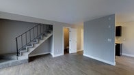 This two-story residence offers a well-designed layout with a focus on clean, modern aesthetics and practical functionality. The main floor features smooth hardwood-style plank flooring in a warm neutral tone, complemented by crisp white trim and cool gray walls that create a bright, contemporary atmosphere throughout.

The open main living area provides a generous sense of space, with clean sightlines that make the floor feel airy and inviting. A conveniently located half bathroom on the main level adds everyday practicality, positioned near additional storage or utility space. White paneled doors throughout contribute to the home's cohesive, polished look.

A staircase with a sleek black metal railing and carpet-covered treads leads to the second floor, serving as both a functional and design-forward element of the interior. The carpeted stairs provide a comfortable transition between levels while the dark metal balusters offer a modern industrial contrast against the neutral palette.

Overall, the space presents a move-in-ready environment with consistent finishes across both levels. The neutral color scheme, durable flooring materials, and thoughtful layout make this a versatile and welcoming home suited to a variety of lifestyles.